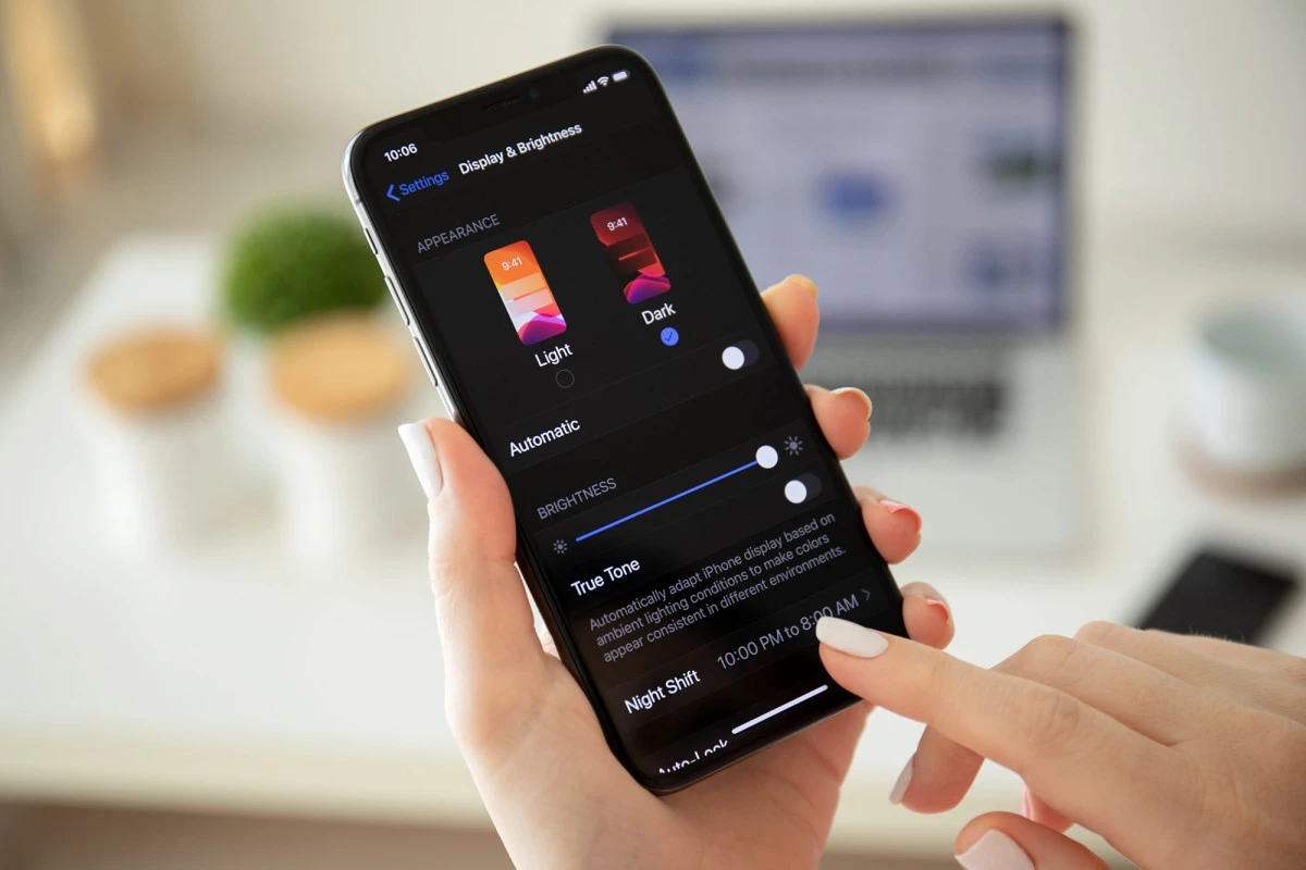 Hand holding an iPhone showing dark mode.