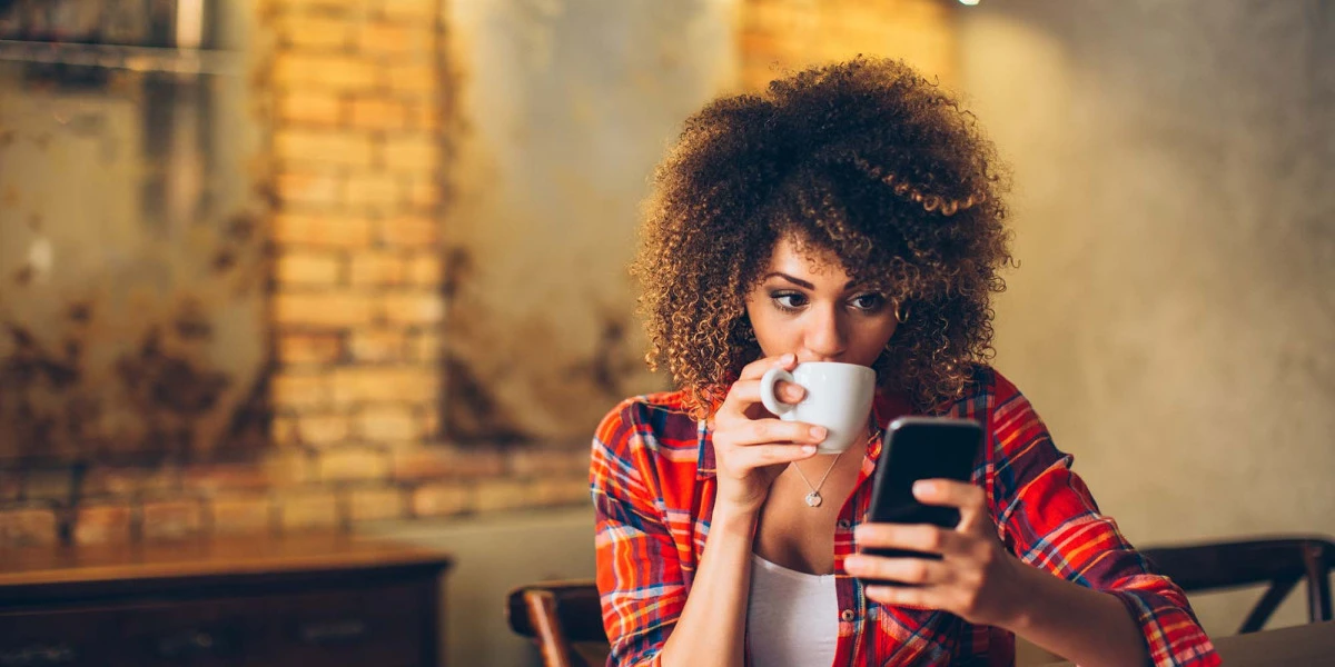 Young woman at cafe drinking coffee and using mobile phone